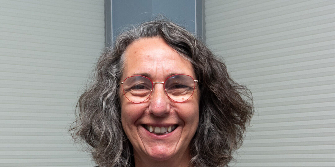 headshot of woman with shoulder length gray hair and red framed glasses