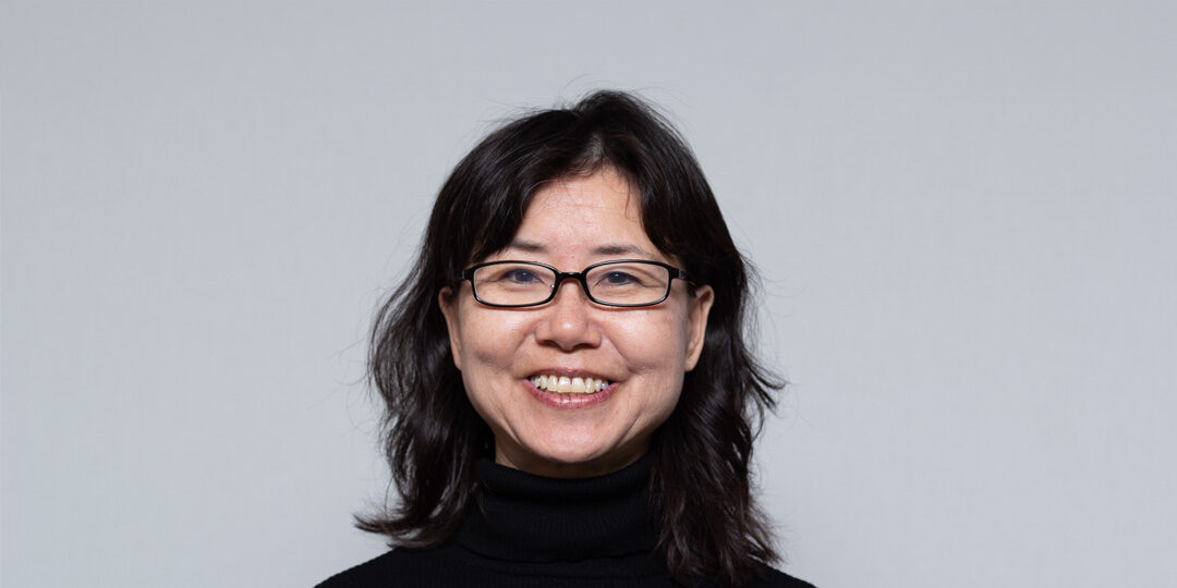 Headshot of woman with shoulder length black hair, black glasses, and black turtleneck