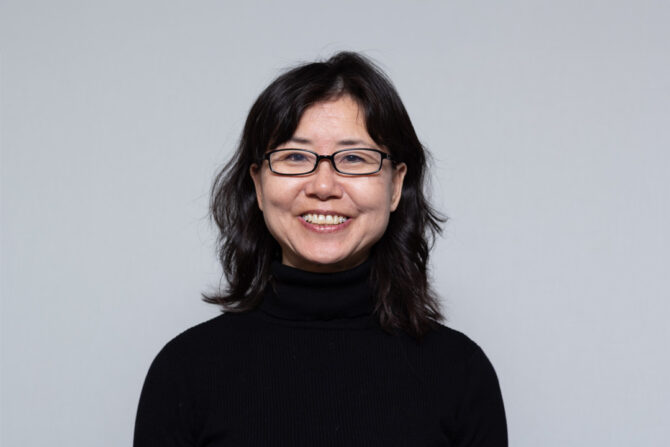 Headshot of woman with shoulder length black hair, black glasses, and black turtleneck