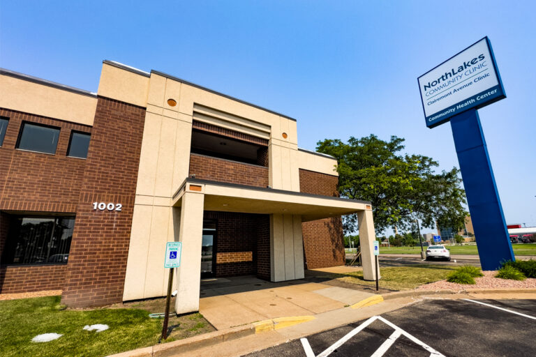 Outside of large brick building with green grass and blue sky. Tall NorthLakes sign in front