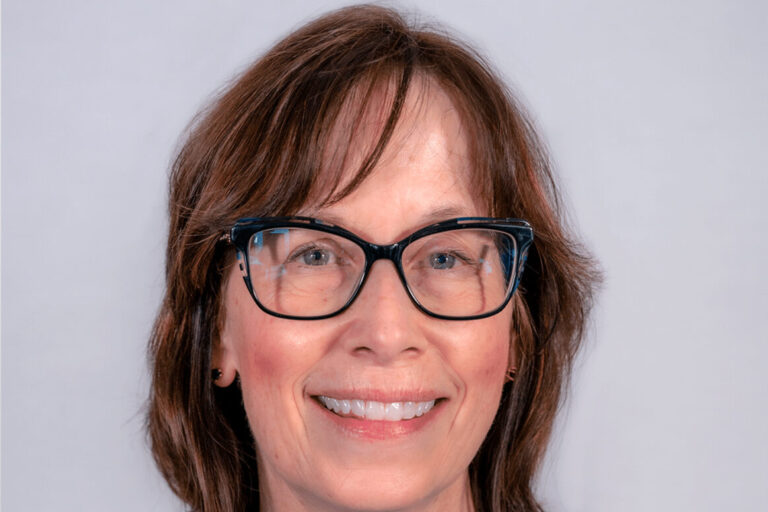 Woman with brown hair, black glasses, and blue blouse