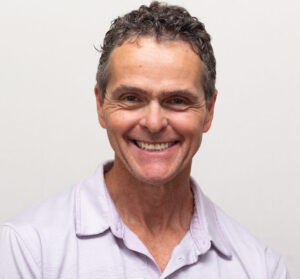 Man with short curly hair and lilac polo 