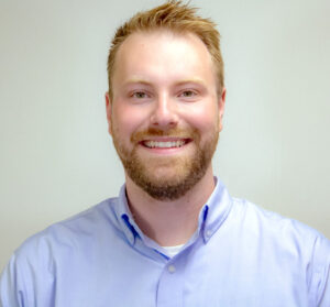 Headshot of man with light blue button up shirt smiling