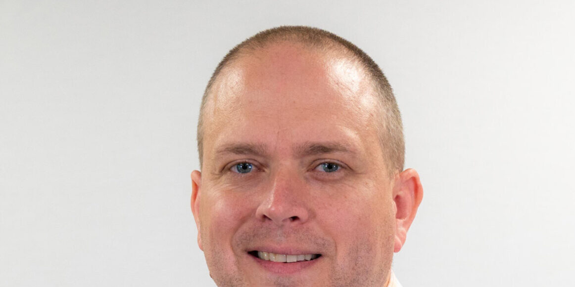 Man with checkered button up and blue eyes smiling