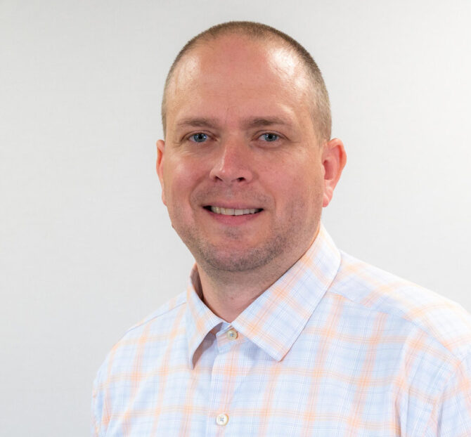 Man with checkered button up and blue eyes smiling