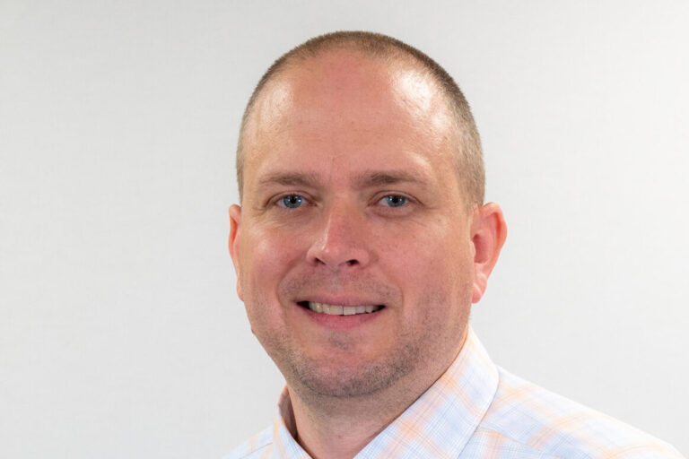Man with checkered button up and blue eyes smiling