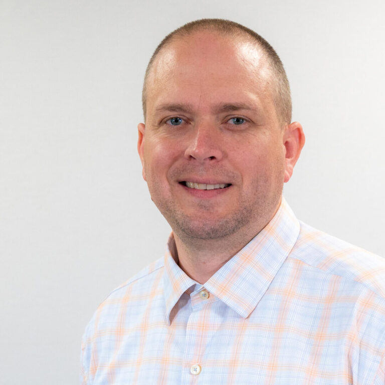 Man with checkered button up and blue eyes smiling