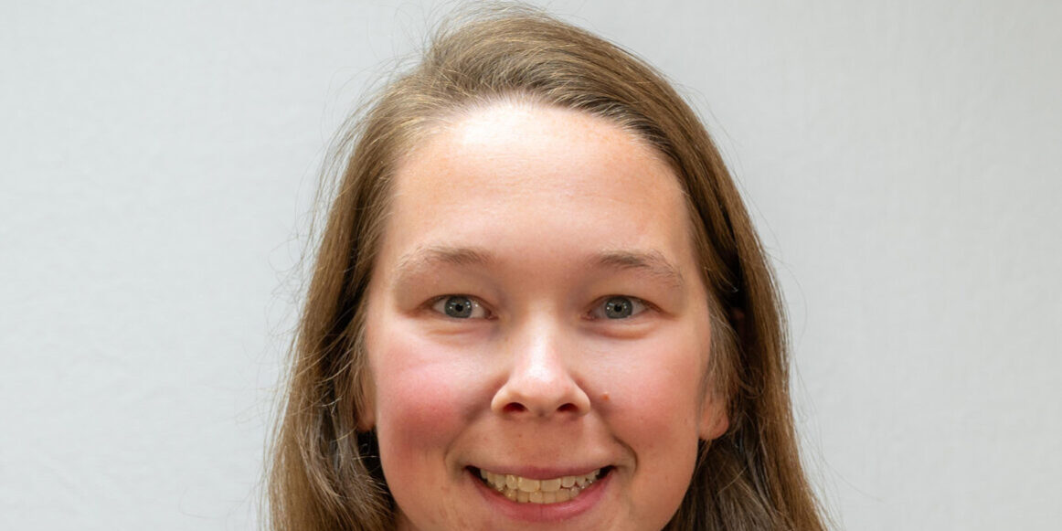 Headshot of woman with long hair and blue top with black jacket