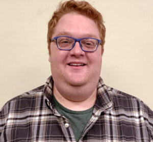 Headshot of man with ginger hair and blue glasses smiling