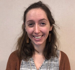 Woman with shoulder length dark hair, earrings, and brown cardigan smiling