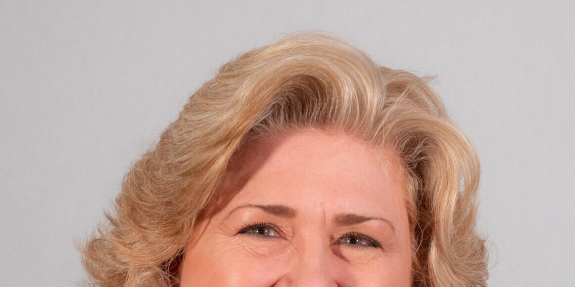 Woman with shoulder length blonde curled hair and black jacket