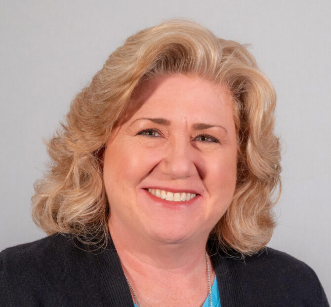 Woman with shoulder length blonde curled hair and black jacket