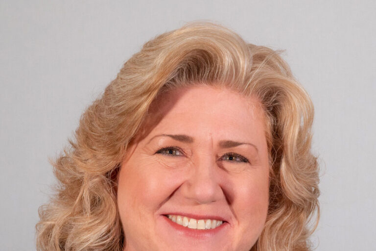 Woman with shoulder length blonde curled hair and black jacket