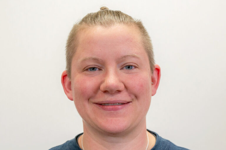 Headshot of person with navy blue waffle shirt, light blue eyes, and blonde hair pulled back into small bun