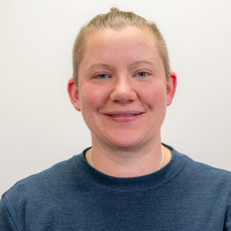 Headshot of person with navy blue waffle shirt, light blue eyes, and blonde hair pulled back into small bun
