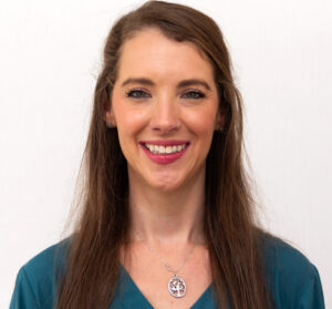 Headshot of woman with dark blue top and long brown hair, smiling with red lipstick