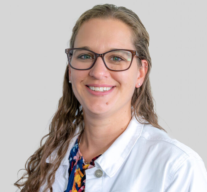 Woman with long hair and glasses heashot wearing a white coat