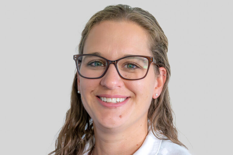Woman with long hair and glasses heashot wearing a white coat