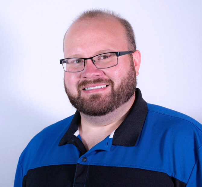 Man with black glasses, brown beard, and polo