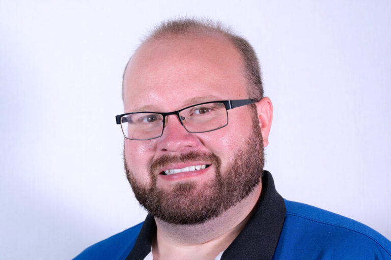 Man with black glasses, brown beard, and polo