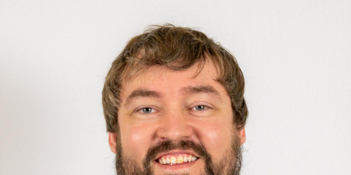 Headshot of man with short brown hair and beard wearing tan polo