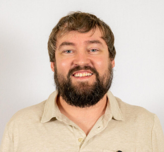 Headshot of man with short brown hair and beard wearing tan polo