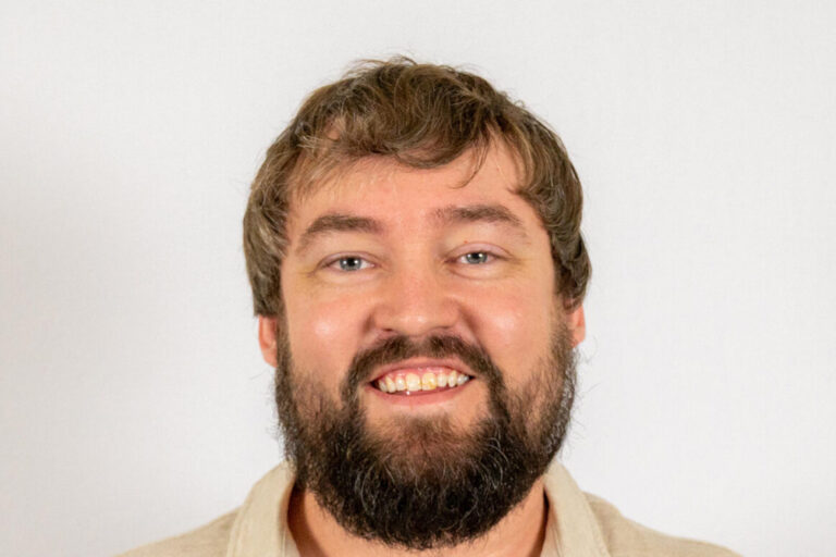 Headshot of man with short brown hair and beard wearing tan polo