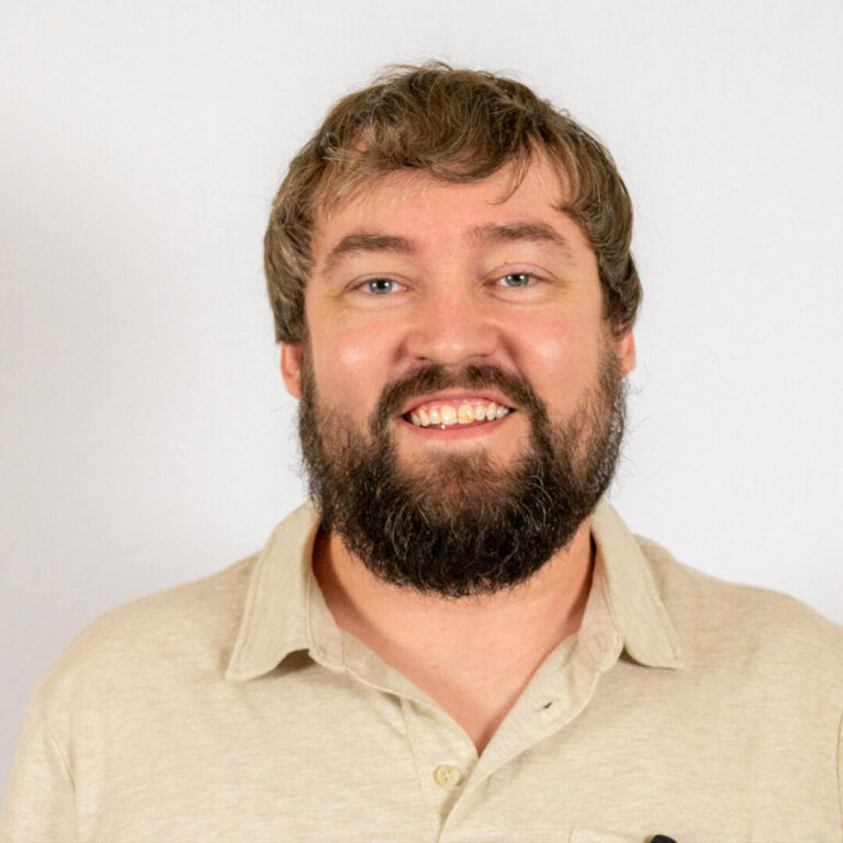 Headshot of man with short brown hair and beard wearing tan polo