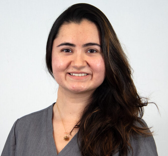 Headshot of woman with long dark hair over one shoulder with gray scrub top