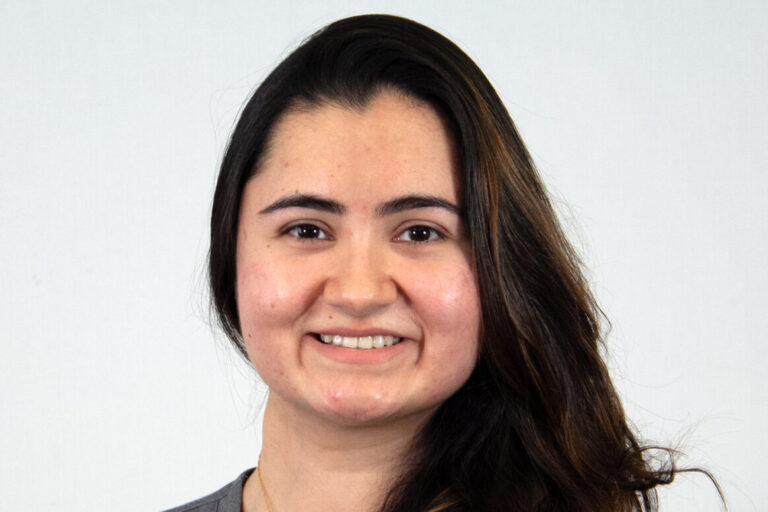 Headshot of woman with long dark hair over one shoulder with gray scrub top
