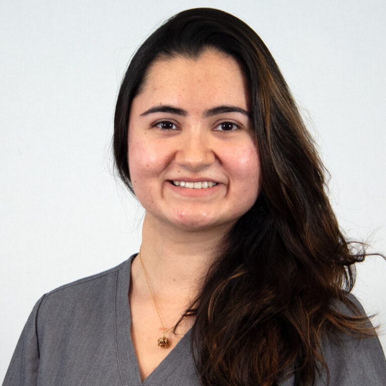 Headshot of woman with long dark hair over one shoulder with gray scrub top