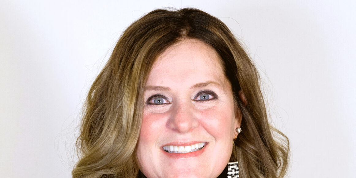 Headshot of woman with long brown hair smiling with a black turtleneck