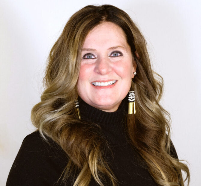 Headshot of woman with long brown hair smiling with a black turtleneck