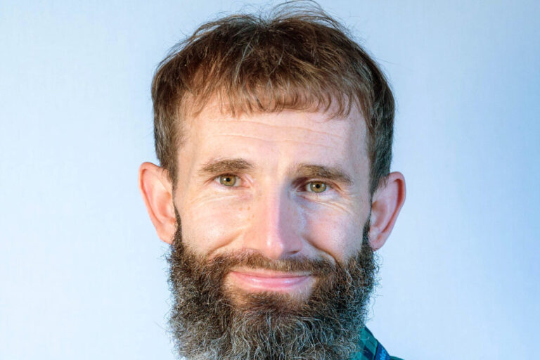 Man with brown hair and beard wearing green and black plaid shirt