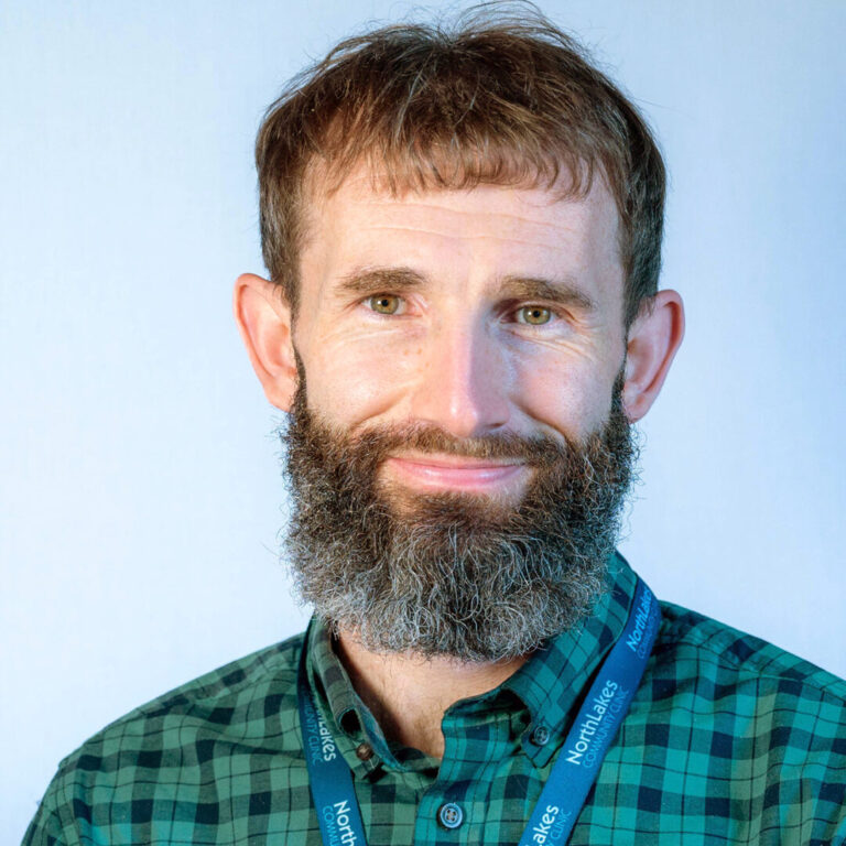 Man with brown hair and beard wearing green and black plaid shirt