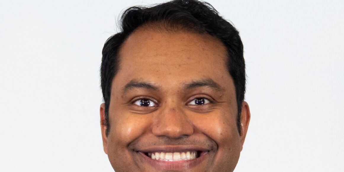 Man smiling with light blue scrubs in studio lighting