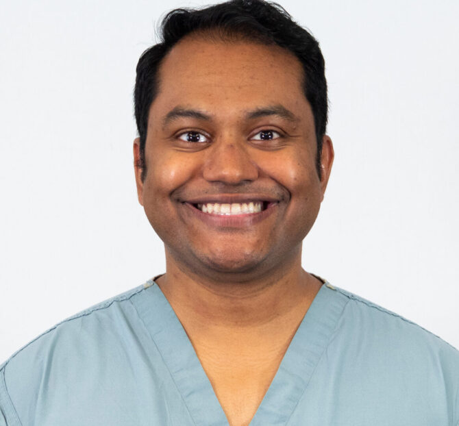Man smiling with light blue scrubs in studio lighting