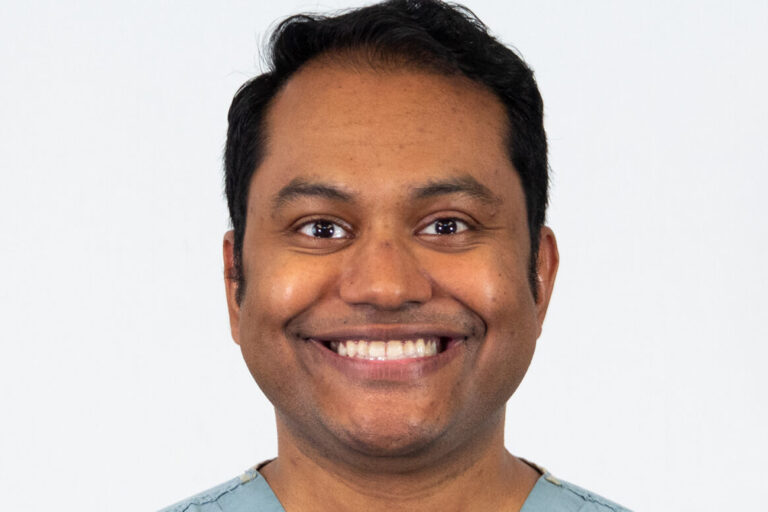 Man smiling with light blue scrubs in studio lighting