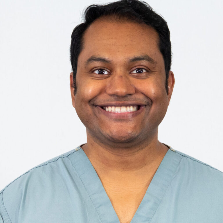 Man smiling with light blue scrubs in studio lighting