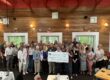 Large group of men and women in resturant around people holding a check for $10,000
