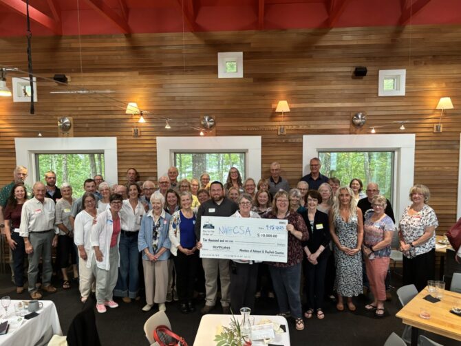 2025 R3 ASHBAY Large group of men and women in resturant around people holding a check for $10,000