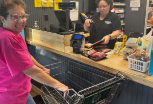 Woman in pink shirt with shopping cart smiling as cashier scans groceries