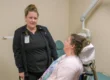 Two people speaking, one standing, and one using a new specialized wheelchair recliner at a NorthLakes dental clinic.